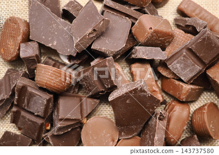 Assorted chocolate pieces scattered on a woven surface Assorted chocolate pieces scattered on a woven surface 143737580