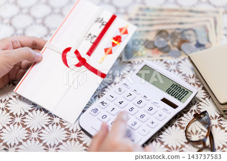 中老年婦女拿著祝賀信封，計算裡面的金額。 143737583