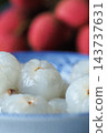 Peeled lychees served in a blue bowl with fruit in the background 143737631