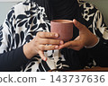 Woman holding a brown cup while wearing a patterned blouse indoors 143737636