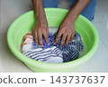 Person washing striped clothes by hand in a green basin 143737637