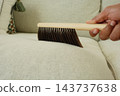 Hand brush sweeping lint from a sofa cushion indoors 143737638