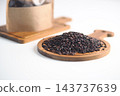 Black rice grains displayed on a round wooden board beside a storage container 143737639