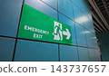 A clearly visible emergency exit sign is mounted on the blue-tiled exterior wall of a building 143737657