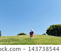 A child runs up a hill in the park, seen from behind, on the grass under a clear sky. 143738544