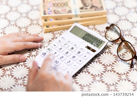 一位中年或老年婦女正在使用計算器來計算金額。 一位中年或老年婦女正在使用計算器來計算金額。 143739254