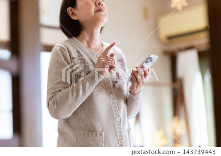 中老年婦女一邊查看智慧型手機,一邊檢查自家房屋的狀況。 中老年婦女一邊查看智慧型手機,一邊檢查自家房屋的狀況。 143739443