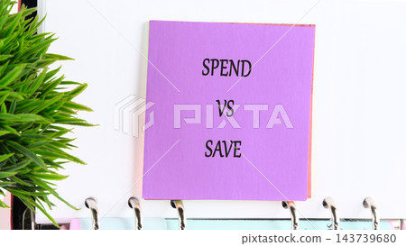 Purple sign with the words spend versus save stands beside a green plant on a shelf in an indoor setting during the day Purple sign with the words spend versus save stands beside a green plant on a shelf in an indoor setting during the day 143739680