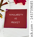A red card marked popularity versus profit rests on a lined planner page beside eyeglasses and a red paper shape 143739685