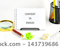A spiral notebook marked content versus design sits on a white desk with a magnifying glass, paper clips, pens, and a calendar page 143739686
