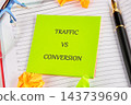 A green note marked traffic versus conversion rests on an open planner with a pen, glasses, and paper clips on a desk 143739690