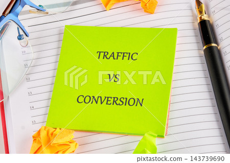 A green note marked traffic versus conversion rests on an open planner with a pen, glasses, and paper clips on a desk A green note marked traffic versus conversion rests on an open planner with a pen, glasses, and paper clips on a desk 143739690