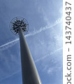 A transmission tower seen against a backdrop of blue sky and contrails. 143740437