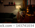 Cozy green sofa under warm lamp stylist staged hygge corner with wood paneling, floating shelf, potted plant, soft cushions, ambient lighting creating intimate mood 143741034