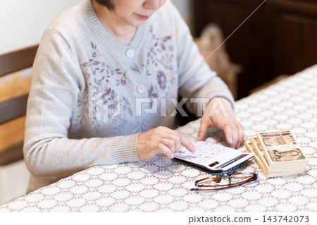 中老年婦女使用計算機計算錢。 中老年婦女使用計算機計算錢。 143742073