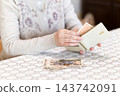 A middle-aged or senior woman's hand taking banknotes out of her wallet. 143742091