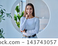 Smiling young female student touching hand to chin in modern campus setting 143743057
