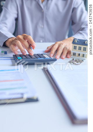 Close-up of accountant hand using calculator with house model and keys on office desk, real estate financial budget concept. 143743656
