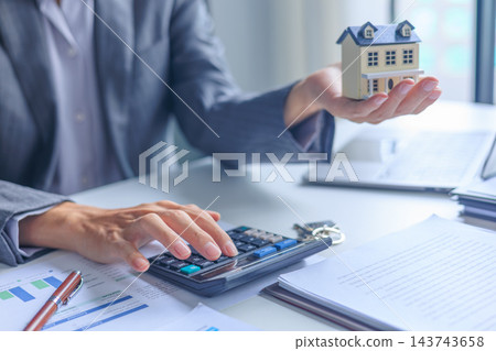 Real estate agent calculating mortgage loan costs with house model and contract on desk. Real estate agent calculating mortgage loan costs with house model and contract on desk. 143743658