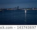 A harbor scene with wind turbines, where the lights of ships sailing in Yokohama Port at night reflect on the water's surface. A harbor scene with wind turbines, where the lights of ships sailing in Yokohama Port at night reflect on the water's surface. 143743697