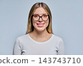 Close-up portrait of smiling young blonde woman in black glasses on grey background 143743710
