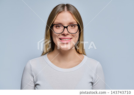 Close-up portrait of smiling young blonde woman in black glasses on grey background 143743710