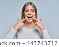 Smiling young woman pointing at her white healthy teeth on grey background 143743712