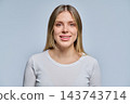 Smiling young blonde woman looking at camera in studio on gray backdrop 143743714