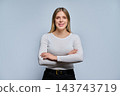 Smiling young woman with arms crossed in studio against grey background 143743719