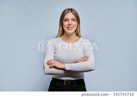 Smiling young woman with arms crossed in studio against grey background Smiling young woman with arms crossed in studio against grey background 143743719