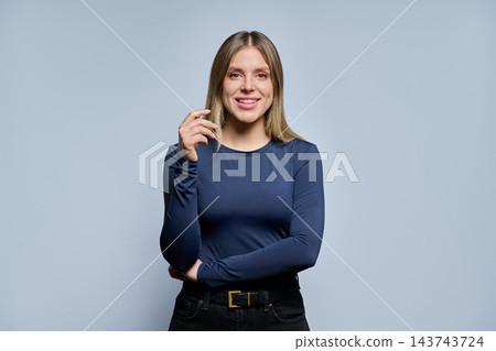 Smiling young woman touch hair and looking at camera in studio portrait Smiling young woman touch hair and looking at camera in studio portrait 143743724