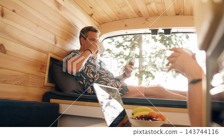 Mature couple enjoying coffee and phone in camper van Mature couple enjoying coffee and phone in camper van 143744116