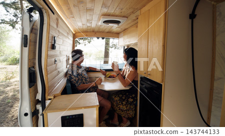 Mature couple enjoying breakfast inside camper van Mature couple enjoying breakfast inside camper van 143744133