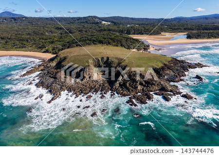 Aerial view of waves breaking around a rocky headland at Sapphire Beach, with a grassy bluff, turquoise water and sandy shoreline near Coffs Harbour, Australia. Aerial view of waves breaking around a rocky headland at Sapphire Beach, with a grassy bluff, turquoise water and sandy shoreline near Coffs Harbour, Australia. 143744476