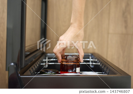 Hand places glass drink bottle inside cooler with other bottles and cans Hand places glass drink bottle inside cooler with other bottles and cans 143746807