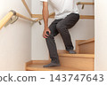 A person holding onto the handrail halfway up the stairs, clutching their knee in pain. 143747643