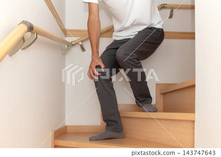 一個人扶著樓梯半腰的扶手，痛苦地摀住膝蓋。 143747643