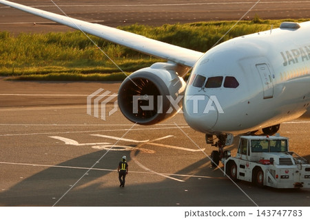 一架客機在夕陽的映照下被推出；一輛牽引車正在將客機推出。 143747783