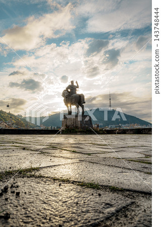 Low angle view of cobblestones leading to a sunlit equestrian statue with Tbilisi TV Tower hill beyond 143748444