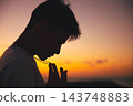 夕陽西下，一位年輕男子側臉祈禱。 143748883