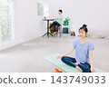 A wife doing yoga in the living room while her husband works in the back. A wife doing yoga in the living room while her husband works in the back. 143749033