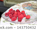 Clear glass plate with ripe red raspberries on a table 143750432