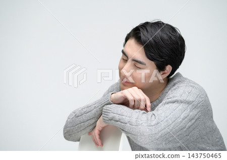 一幅日本男子的肖像,他身穿灰色針織毛衣,雙臂搭在椅子上,雙眼緊閉。 一幅日本男子的肖像,他身穿灰色針織毛衣,雙臂搭在椅子上,雙眼緊閉。 143750465