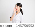 美容診所的一名女工作人員身穿白色醫護服，面帶微笑，一邊用手摀住嘴一邊喊叫。 143750552