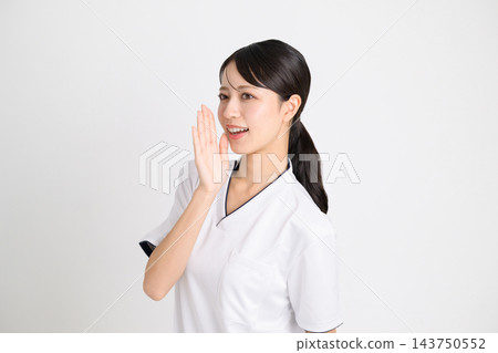 美容診所的一名女工作人員身穿白色醫護服,面帶微笑,一邊用手摀住嘴一邊喊叫。 美容診所的一名女工作人員身穿白色醫護服,面帶微笑,一邊用手摀住嘴一邊喊叫。 143750552