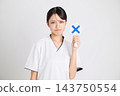 美容診所的一名女工作人員，身穿白色醫療制服，舉著一個「X」標誌。 143750554