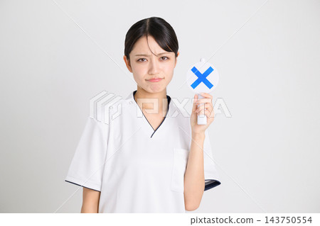 美容診所的一名女工作人員,身穿白色醫療制服,舉著一個「X」標誌。 美容診所的一名女工作人員,身穿白色醫療制服,舉著一個「X」標誌。 143750554
