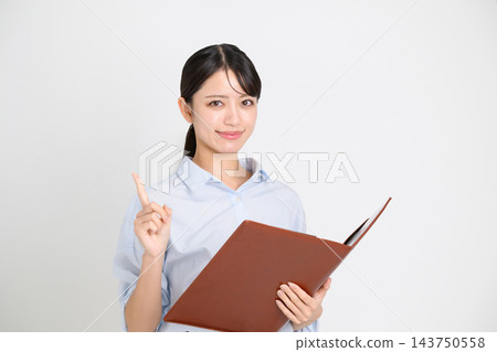一位身穿淺藍色襯衫的女商人,手裡拿著一個棕色文件夾,面帶微笑,舉起食指指出一個關鍵細節。 一位身穿淺藍色襯衫的女商人,手裡拿著一個棕色文件夾,面帶微笑,舉起食指指出一個關鍵細節。 143750558