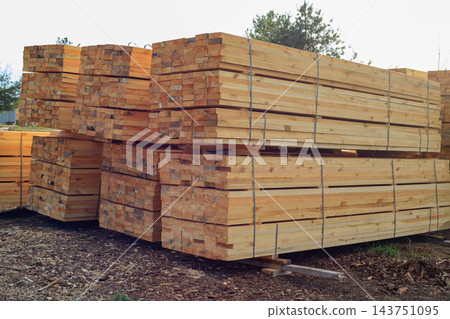 Wooden boards stacked and bound together at an outdoor construction site. Freshly cut timber planks for construction and manufacturing Wooden boards stacked and bound together at an outdoor construction site. Freshly cut timber planks for construction and manufacturing 143751095