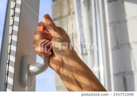 Elderly person closes the handle of a uPVC window to improve energy efficiency and thermal insulation in the home. Protecting against drafts is a way to retain heat and ensure comfort indoors Elderly person closes the handle of a uPVC window to improve energy efficiency and thermal insulation in the home. Protecting against drafts is a way to retain heat and ensure comfort indoors 143751096